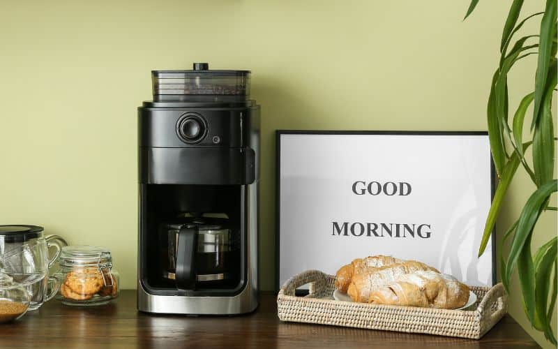 A coffee machine on a counter top with a tray of bread and cups on the other side