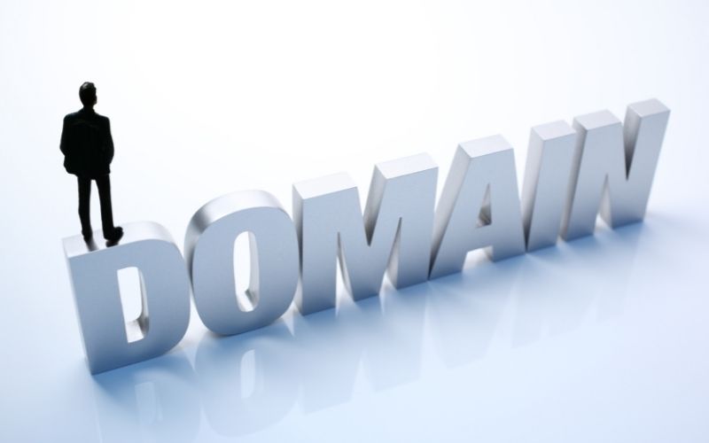 toy businessman standing on top of block letter word domain 