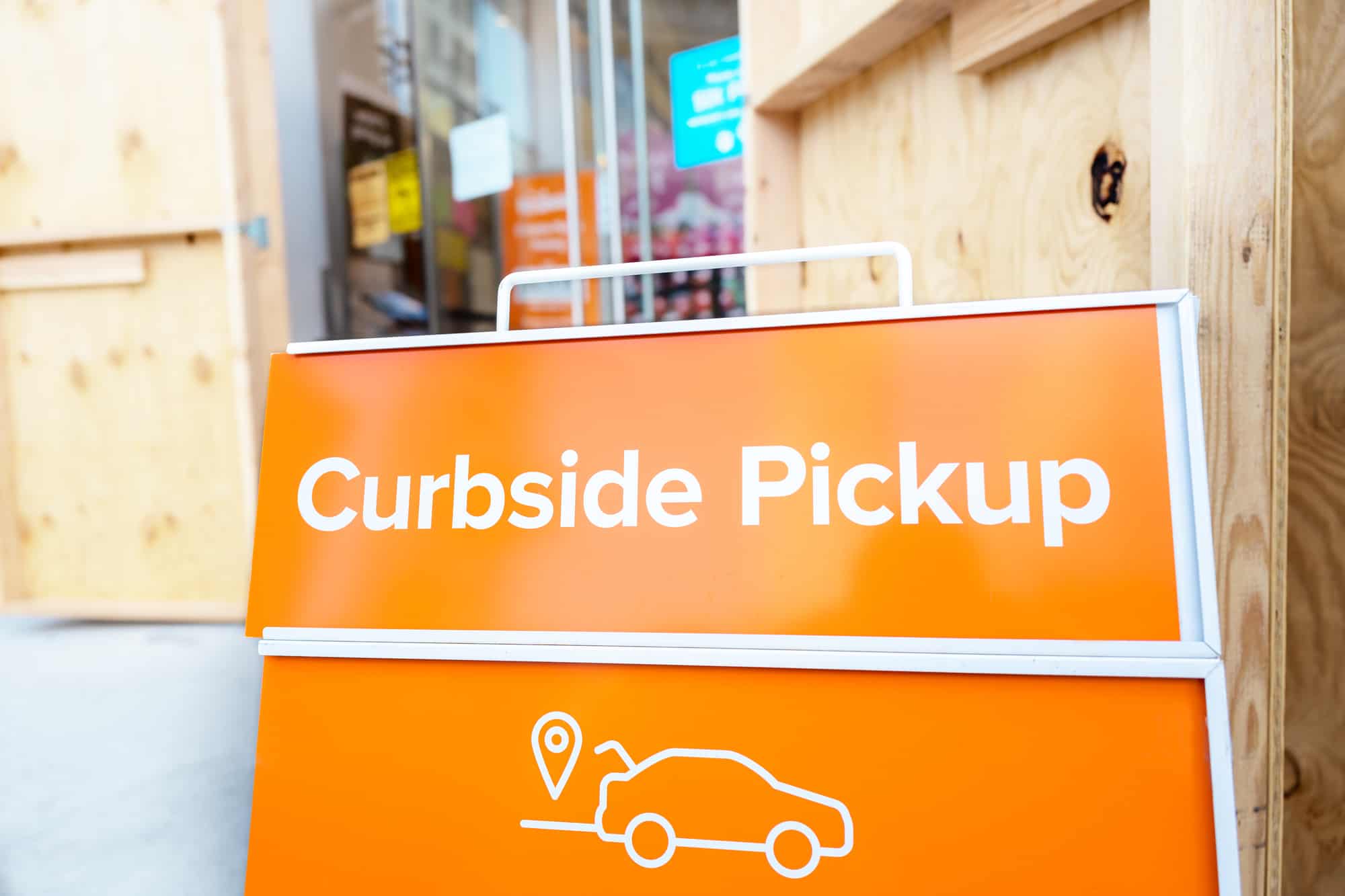 A light orange signage in a street in front of the store which reads curbside pickup