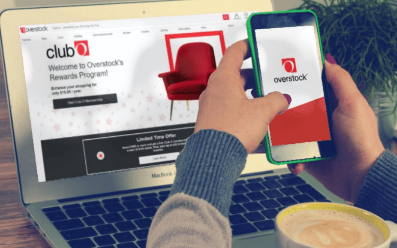 Image showing a hand holding a smartphone in front of a laptop with Overstock website